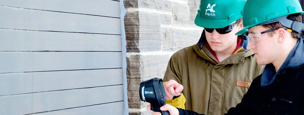 Two male appearing students examining a building with infrared scanners.