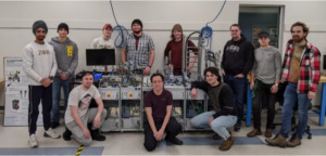 group shot of engineering students posed around a work table filled with engineering tools and equipment