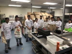 Algonquin College culinary students stand together in a row wearing their chef whites for a picture in one of AC's industrial kitchens.
