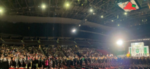 wide shot of group of graduates standing facing the podium at the Canadian Tire Centre