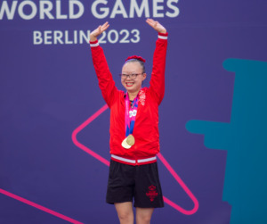 Kimana Mar holds up her hands in celebration at the Special Olympic World Summer Games in Berlin. Mar wears a red, Team Canada jacket, her medals and a smile. 