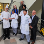 Group shot of culinary arts faculty on stairs in H building holding jar are crab apple butter