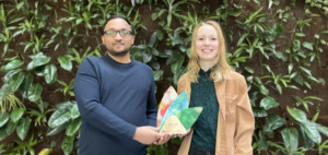 Male and female hold prize in front of living wall at Algonquin College