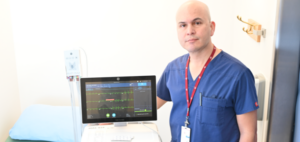 Profile of Fernando Castellanos wearing hospital scrubs next to an ECG machine, 