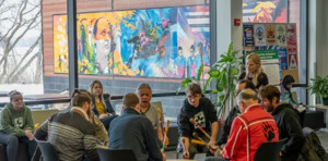 group of students gathered around an elder playing a traditional drum