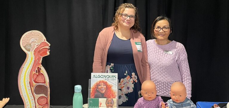 A faculty member and alumna of the Bachelor of Science in Nursing program pose with their table setup at the event. 