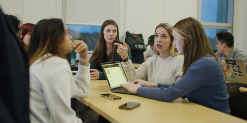 Students in the Bachelor of Commerce Marketing program engaged in class sitting at a long table with their laptops open and typing.