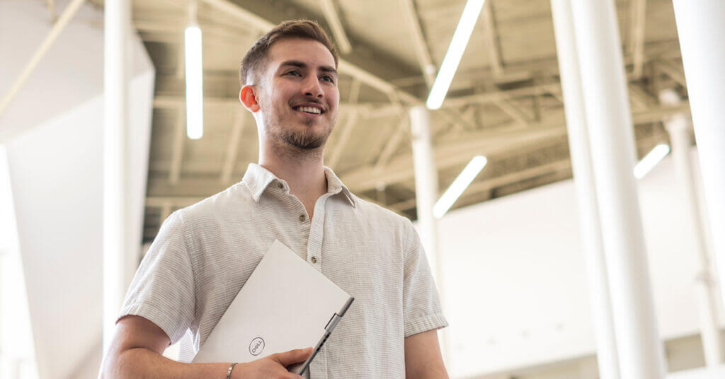 Male student at campus walking holding a laptop.