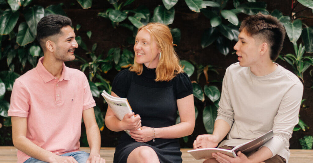 Three students sitting in atrium and talking.