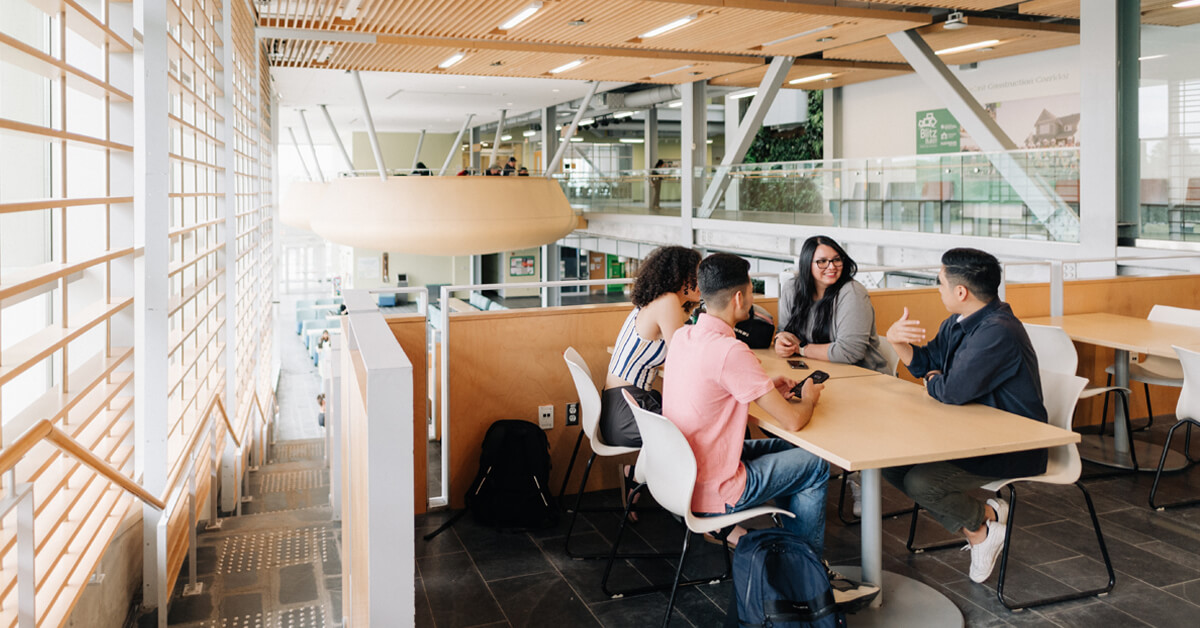 Four students sit around a table talking in the Algonquin Centre for Construction Excellence building.