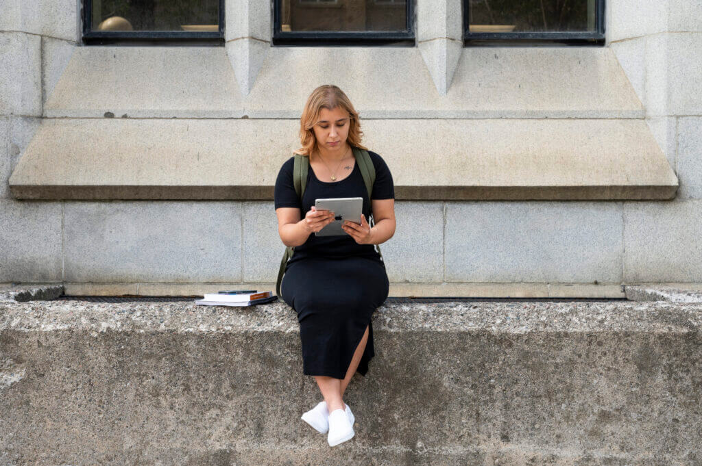 AC Online alumna sits outside on a concrete step looking at her tanlet