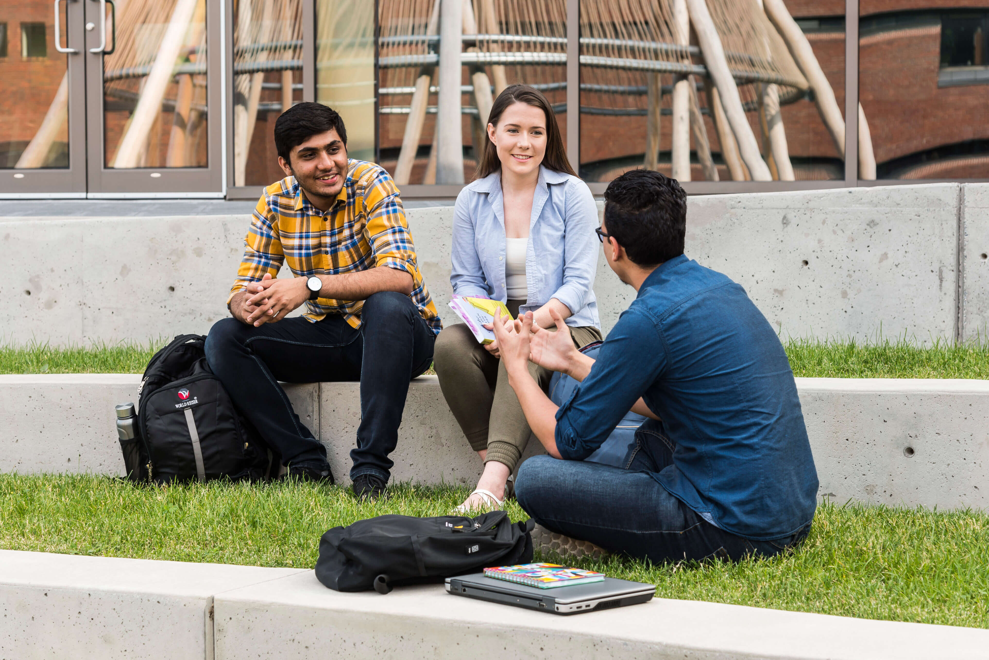 Three young adults are smiling and talking to each other in the Ishkodewan courtyard at Algonquin College.
