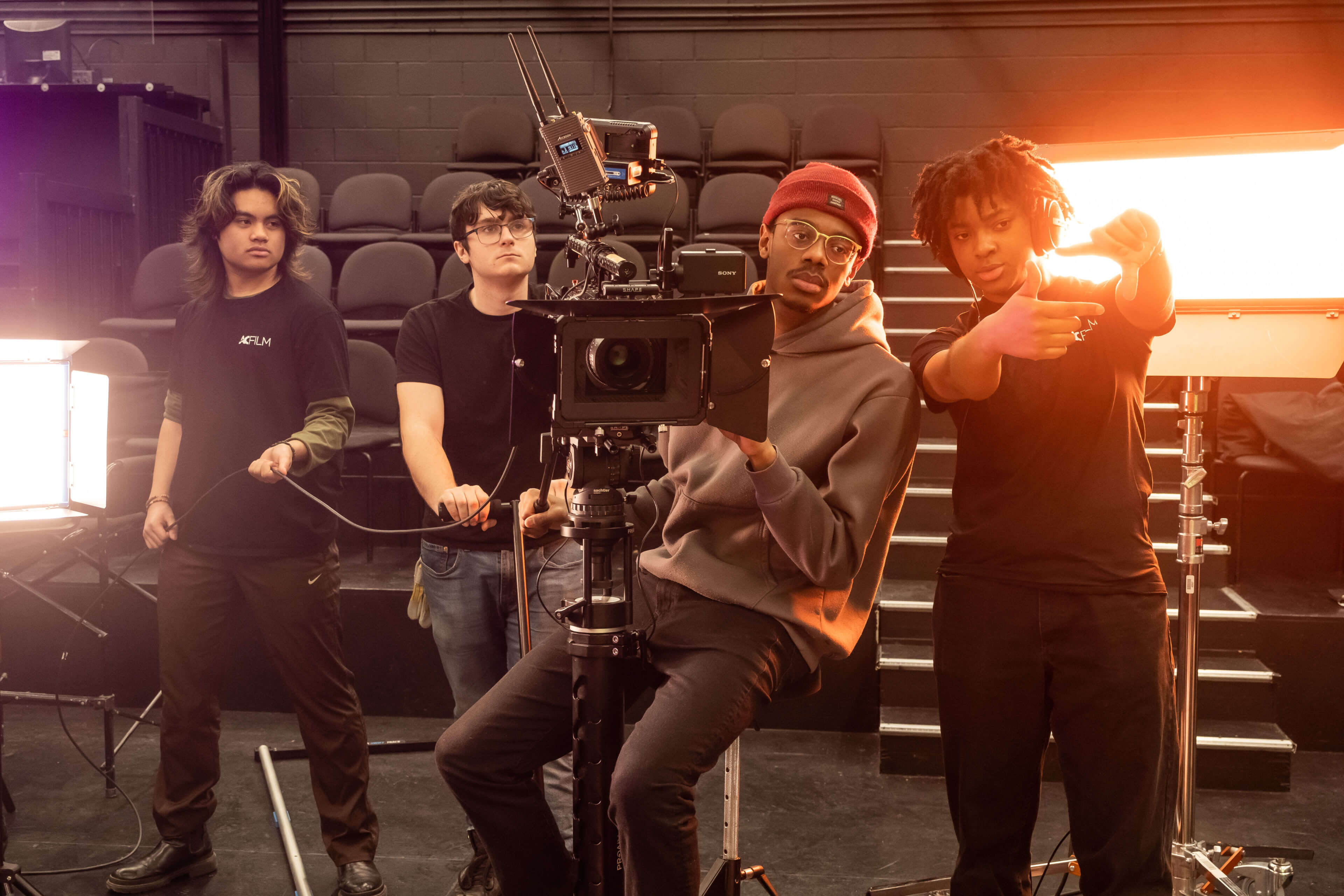 Four crew members on a film set, with one person operating a large camera and others assisting with lighting and photography.