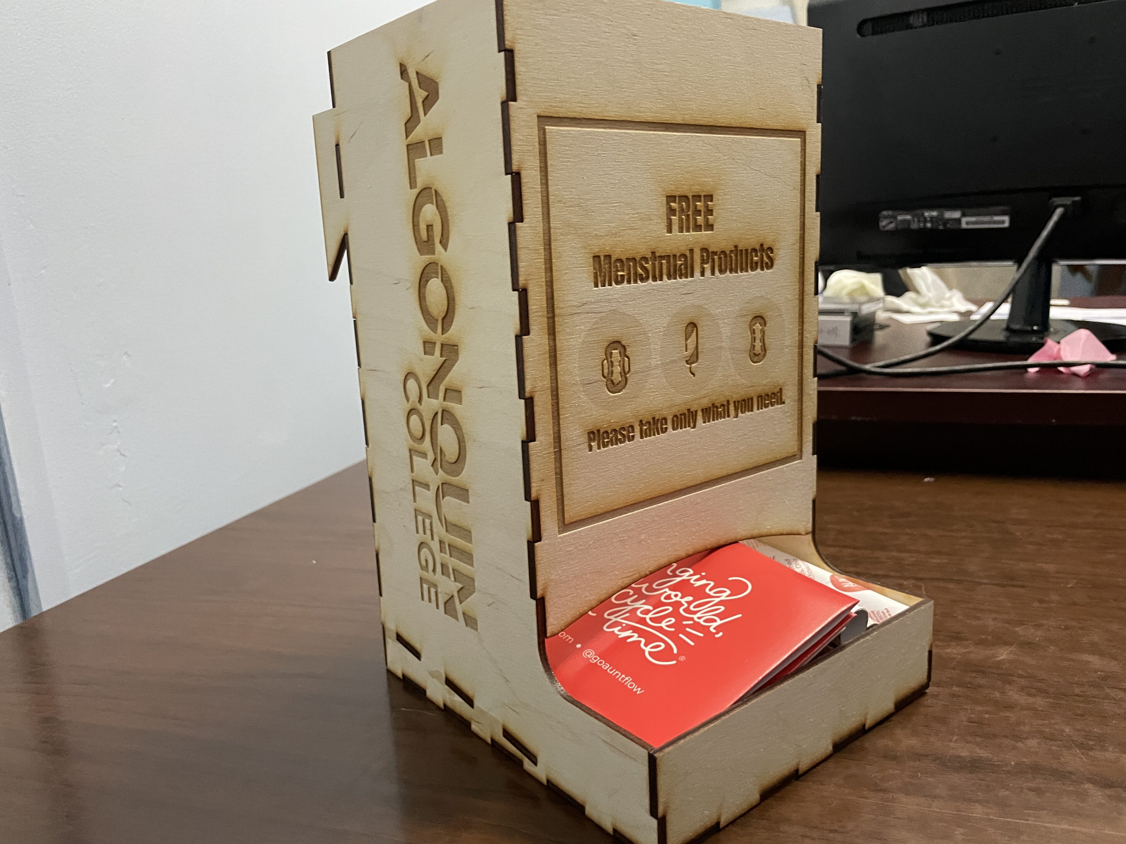 A wooden box with a red menstrual hygiene product box in it